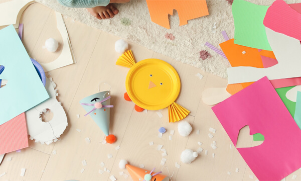 A table covered with Easter crafts - centre-frame is a chick made from a yellow paper plate