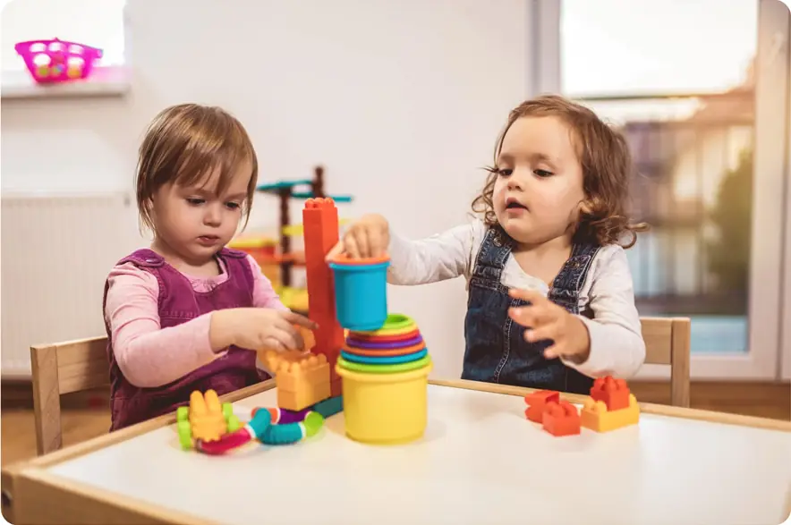 Two children playing with stacking cups on a child's table