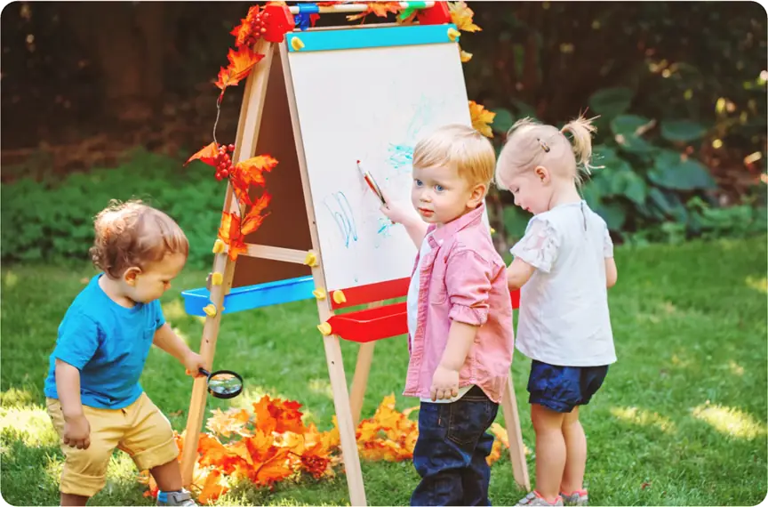 Ofsted Activities to expect image - children playing outside with a paper flipchart and painting on it or looking at leaves