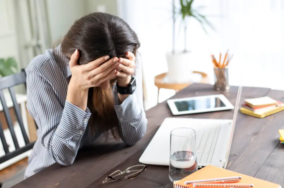 A woman sat at a desk at home, strewn with office paraphernalia, with her head in her hands. Frustrated at funding rules perhaps