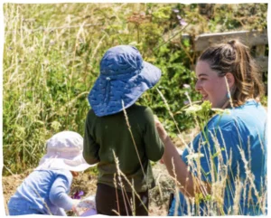 The Pheasant Nest Exceptional Inclusion Image - Child in hat in long grass with educator alongside