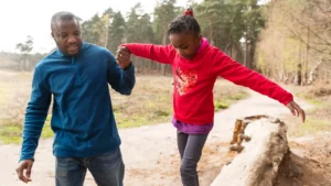 Buitenspelen: meisje balanceert op een boomstam in het bos terwijl een volwassene haar een hand geeft