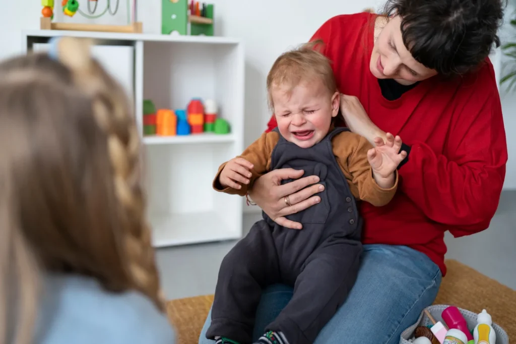 Driftbui peuter: pedagogisch professional houdt een huilende peuter rustig vast op schoot