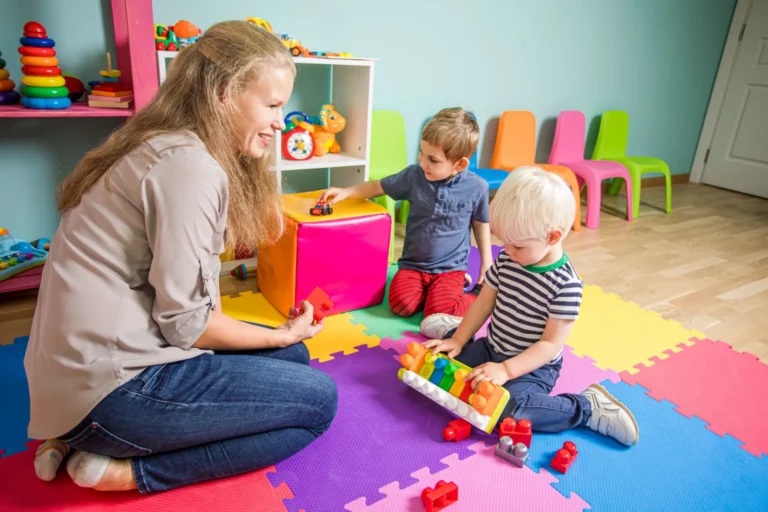Hechting in de kinderopvang: pedagogisch professional speelt op de grond met twee peuters